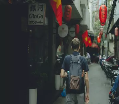 A man walking down a narrow alleyway in Ho Chi Minh with red lanterns hanging from the ceiling.
