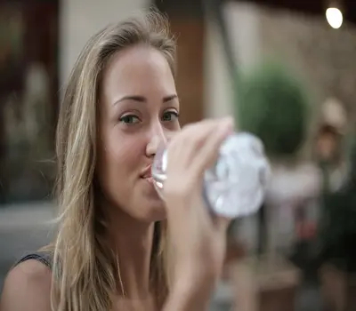  Focus photo of smiling woman drinking water from a plastic bottle.