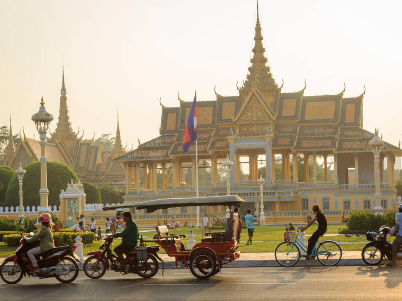 Cyclists and tuk-tuks passing by a grand palace during sunset 