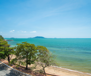 Clear blue waters meeting a quiet sandy shoreline, bordered by lush green trees under a sunny sky in Cambodia