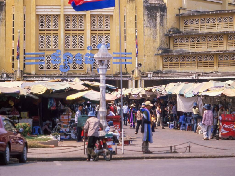 Bustling market scene with colorful stalls and a historic yellow building 