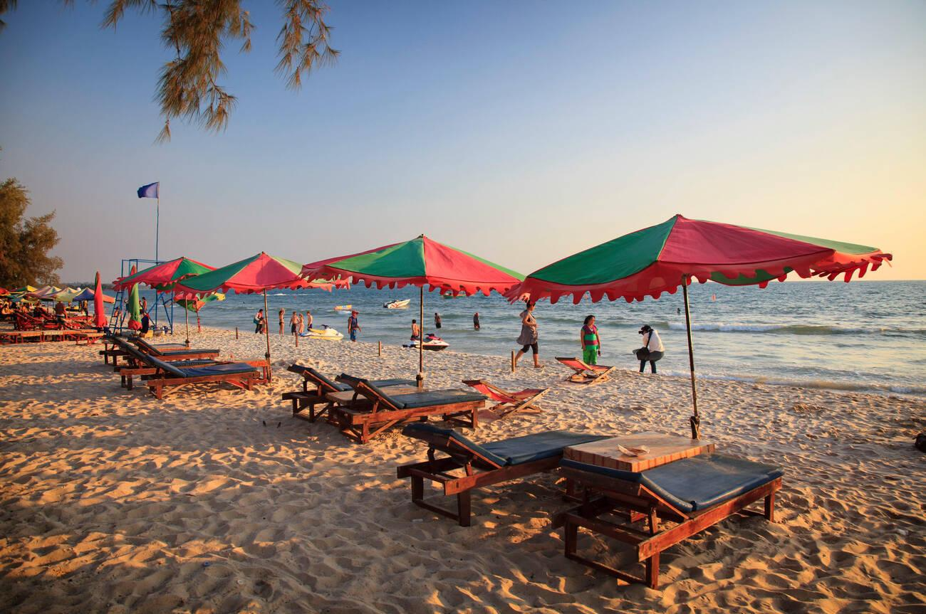4 - Travelpreneur A beach with colorful umbrellas and wooden lounge chairs under the sunset