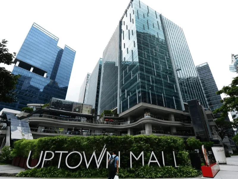 Glass-walled Uptown Mall exterior surrounded by greenery and skyscrapers
