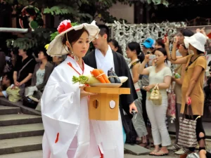 A Japanese bride in a white kimono carrying ceremonial offerings during a traditional wedding ceremony.