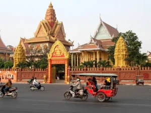Vibrant streets of Phnom Penh with tuk-tuks passing in front of Wat Phnom’s golden gates