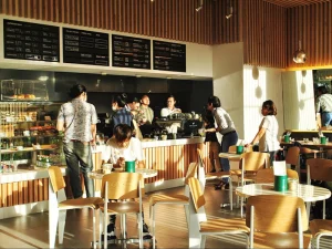 Sunlit coffee shop with customers ordering and chatting at tables.