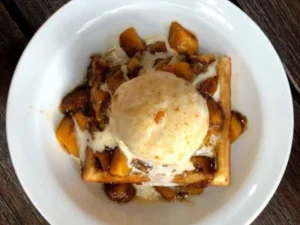 Caramelized banana waffle topped with vanilla ice cream on plate.