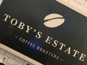 Toby’s Estate Coffee Roasters logo sign on black wall.