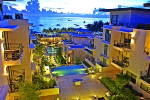 discovery boracay hotel - Travelpreneur A luxurious beachfront resort at twilight, featuring modern architecture, multiple pools, and a stunning ocean view with boats in the distance.