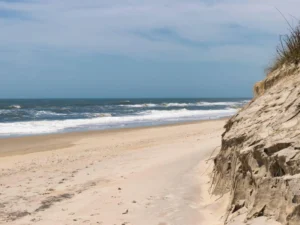Steep sandy dunes beside rolling waves and open blue sea