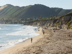 People stroll along beach beneath steep scenic coastal cliffs
