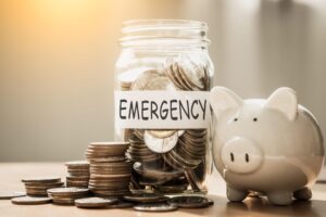 A lot coins in glass money with piggy bank for saving emergency moneySaving for emergency concept - Travelpreneur a poggy bank and a jar full of coins labelled as emergency