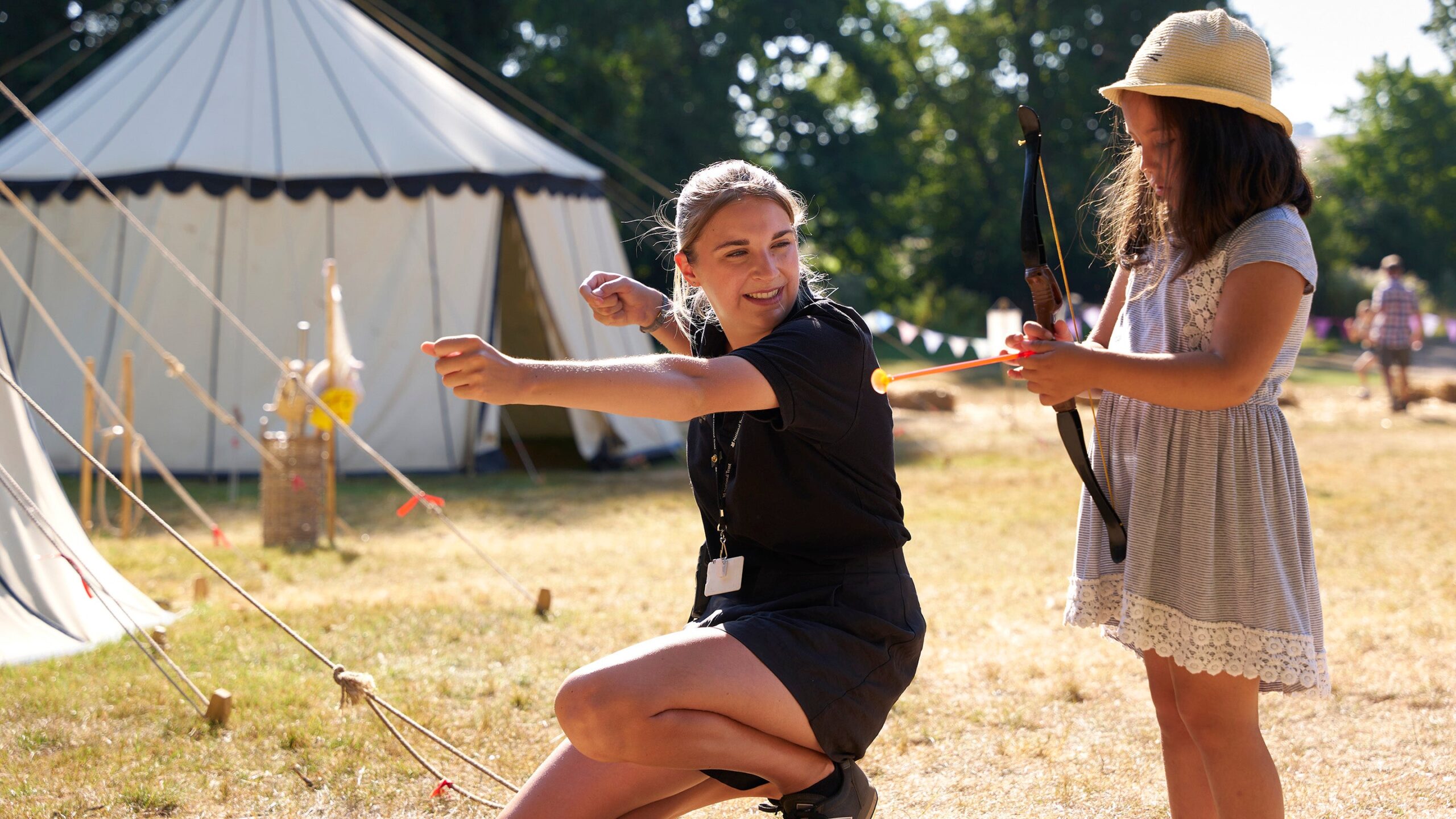 A castle staff teaching a young girl archery at the medieval bodiam fair