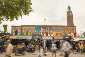 busy norwich market with people strolling along and interacting with vendors