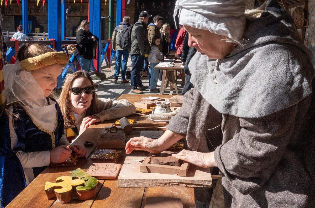 The visitor interacting and participating at a craft booth with a staff dressed in medieval clothes during a castle event at Alnwick Castle Interactive Exhibits