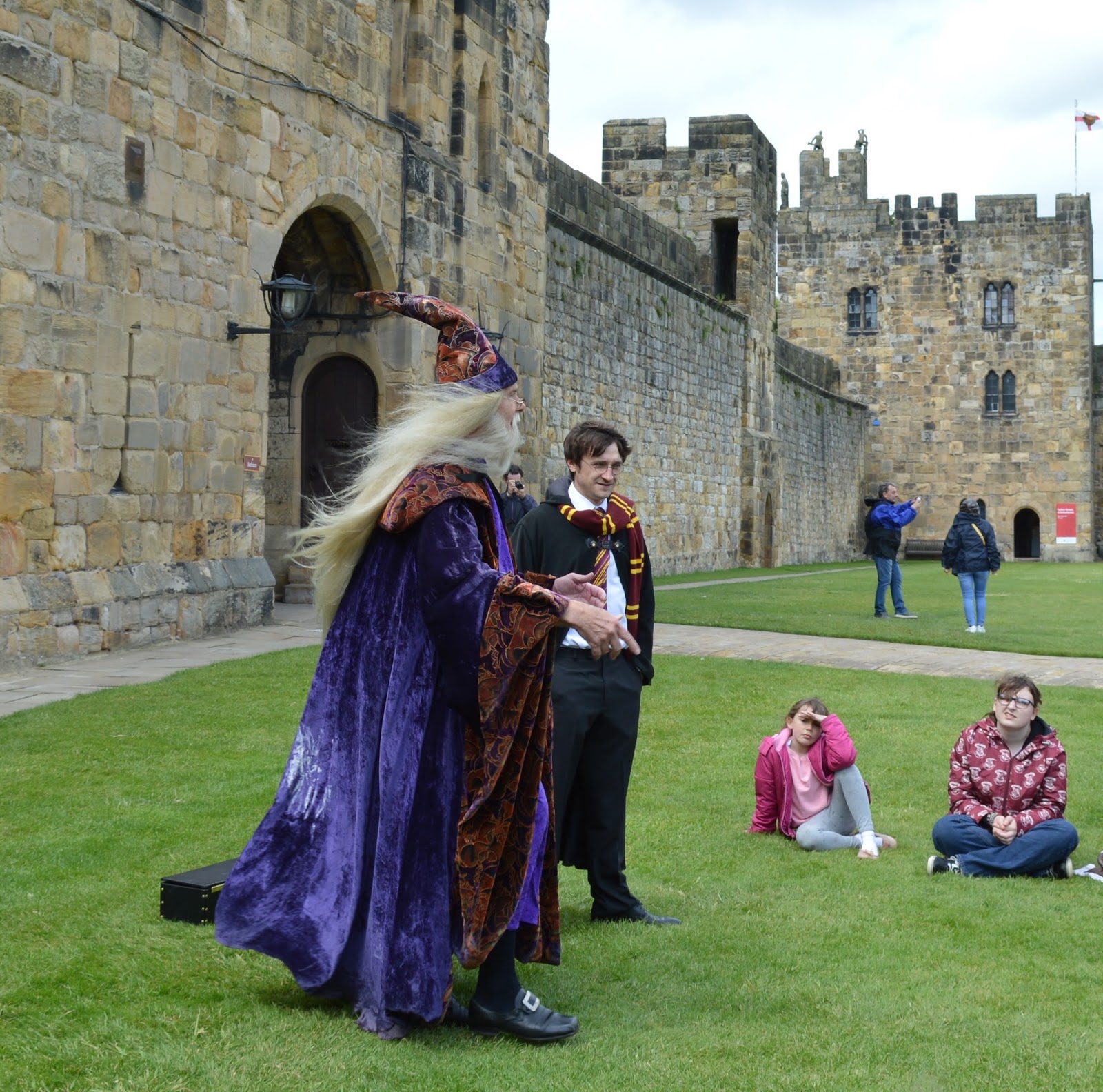 Alnwick Castle with two staff dressed as harry and dumbledore speaking to the visitor on the castle ground during a Harry Potter themed Tour