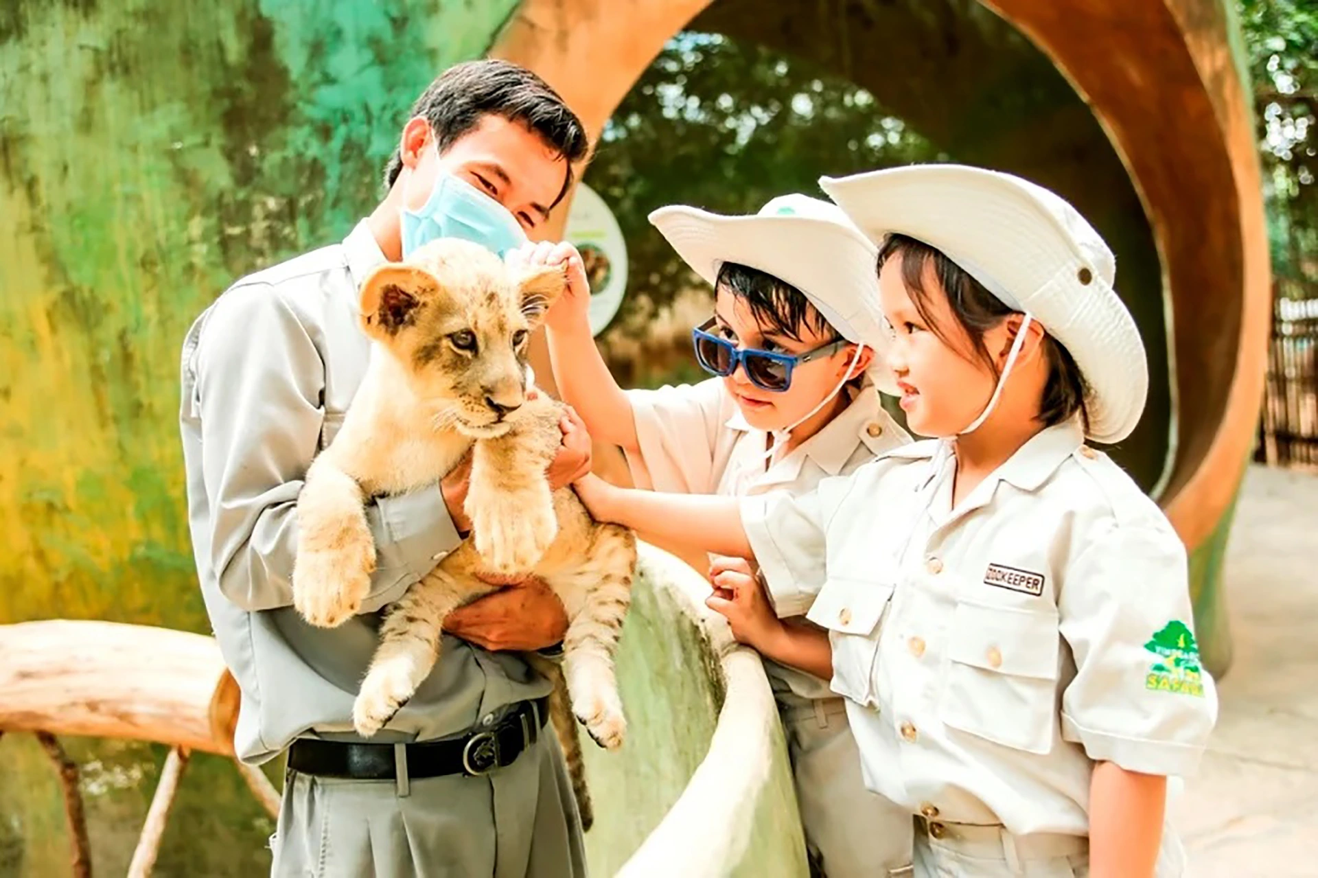 Children gently petting the lion cub help by a zoo keeper at Vinpearl Safari