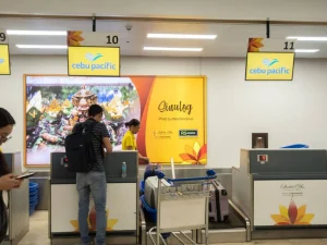 Travelers check in at Cebu Pacific airport counter with festival signage, illustrating domestic tourism activity