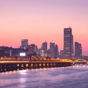 City skyline and bridge lights at sunset over river, highlighting urban tourism growth across Asia