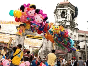 Vendors hold colorful character balloons near old church, Holidays in the Philippines fiesta crowd walking