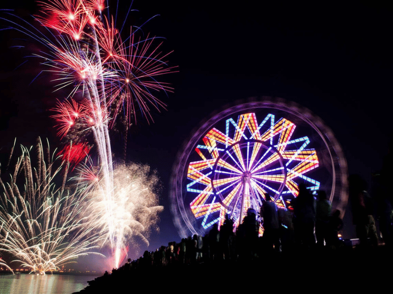 Fireworks burst beside glowing ferris wheel, Holidays in the Philippines night celebration silhouettes watch waterfront