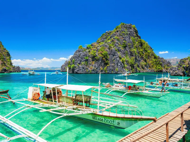 Outrigger boats float on clear lagoon near limestone island, Holidays in the Philippines snorkeling stop