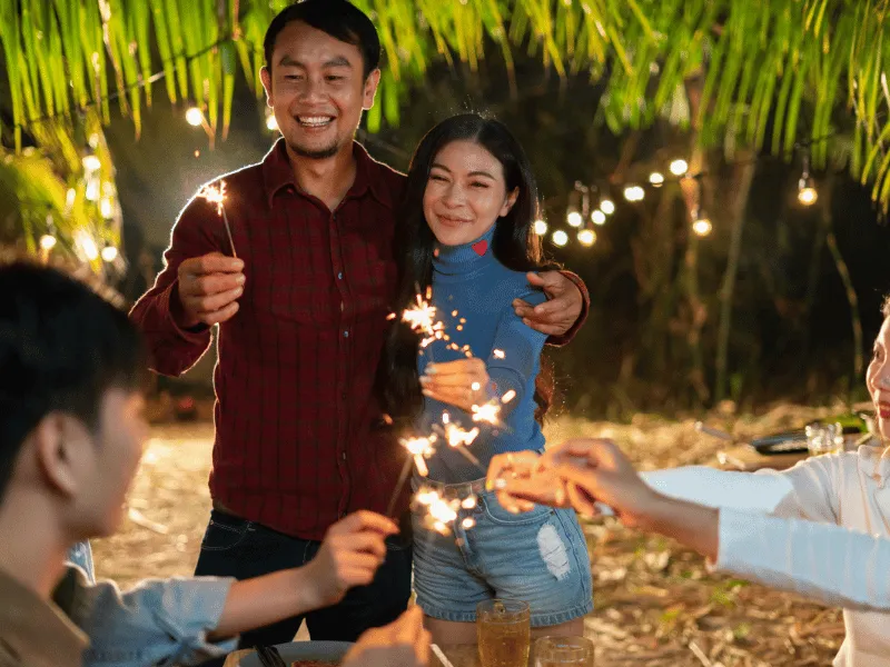 Friends celebrate outdoors with sparklers at night, smiling couple, Holidays in the Philippines party moment