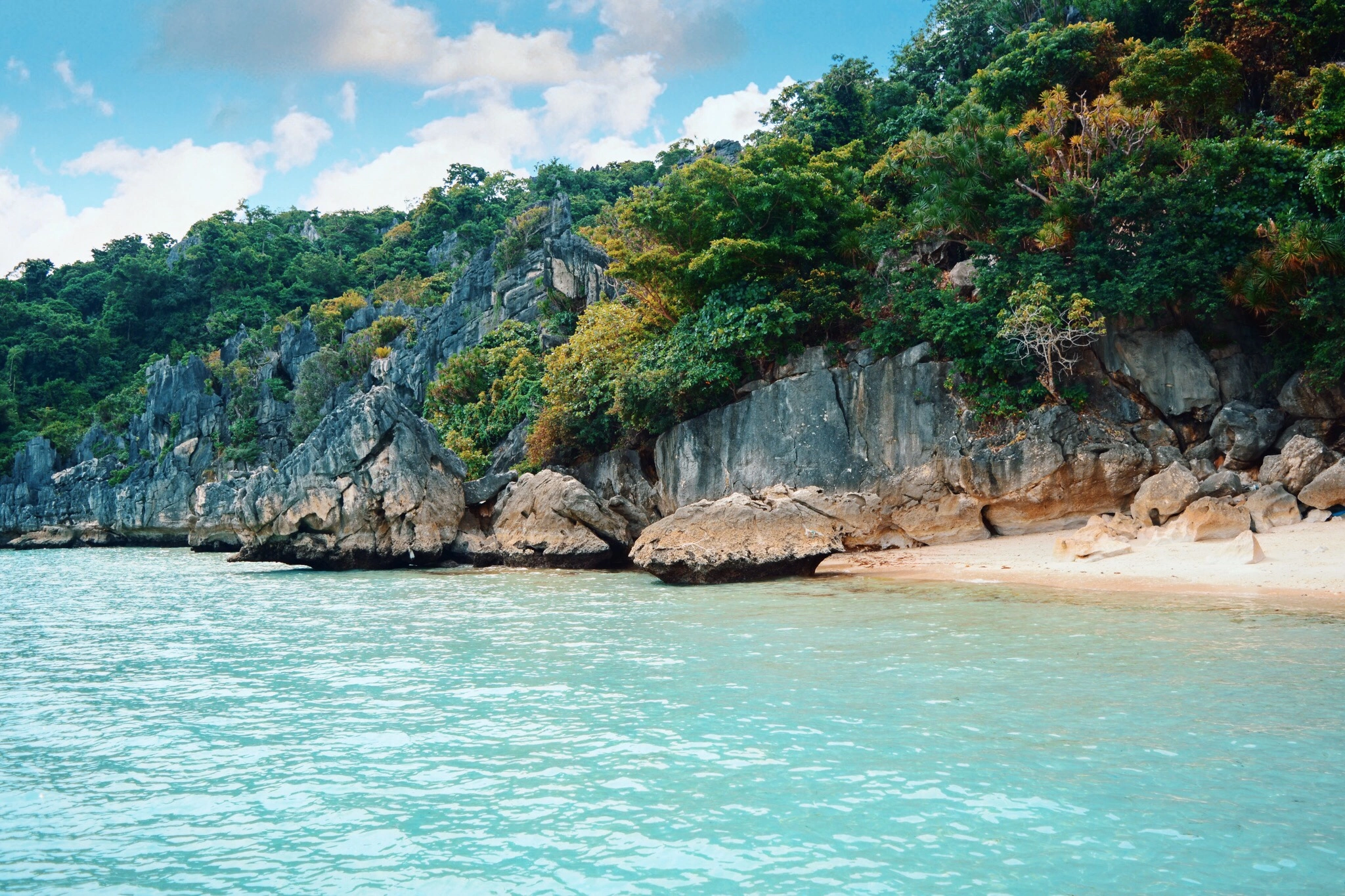 Puting Baybay Beach in Islas de Gigantes, Iloilo - Travelpreneur A secluded cove at Puting Baybay Beach showing a small stretch of white sand, dramatic gray karst limestone cliffs, and lush green trees bordering bright turquoise ocean water.