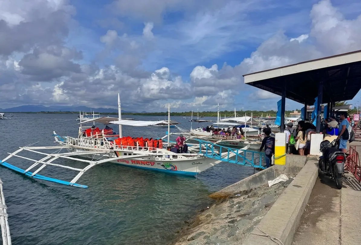 Traditional Filipino outrigger boats, or bangkas, docked at Estancia Port terminal in Iloilo with passengers waiting to board for Gigantes Island.